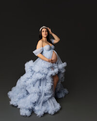 Expecting mother wearing a light blue ruffle maternity gown and crown during a dramatic studio maternity photography session by Kaitlyn Dawn Photography.