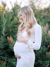 An expecting mom dressed in white standing in front of a flowering tree