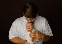 Father gently kissing his newborn baby during a cozy family portrait. Photographed by Inland Empire newborn photographer Kaitlyn Dawn Photography.