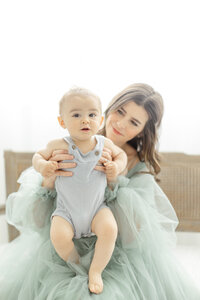Beautiful light filled in studio photo of a mother holding her baby boy for his milestone pictures.