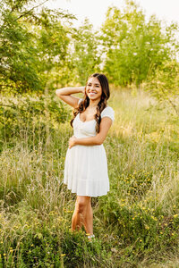 high school senior girl in a stylish short white dress, gently holding her hair back and smiling for Green Bay senior photo session