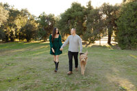 Couple walking their dog through a grassy park during golden hour, candid outdoor family and pet portrait by Kaitlyn Dawn Photography.