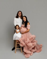 Studio maternity family portrait of expecting mother in a pink gown with partner and young daughter photographed by Kaitlyn Dawn Photography.