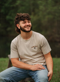 Senior portrait at Circle B Lake in Wilmer, Alabama — sitting on a wooden bench in jeans and a
T-shirt, looking off into the distance.