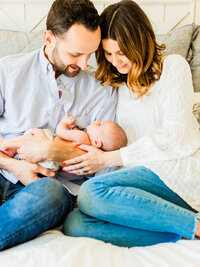 Mother and father sitting together and smiling down at their newborn baby during a relaxed in-home lifestyle newborn session.