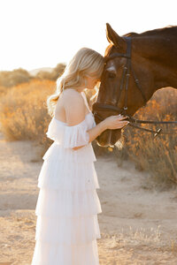 High school senior girl standing beside a horse during golden hour in a field, natural light senior portrait by Kaitlyn Dawn Photography.