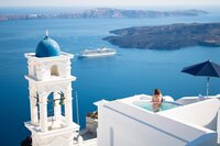 Traveler soaking in a bathtub with a view of Santorini’s blue domes and the Aegean Sea.
