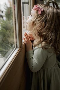 A toddler girl presses her face up against the reflection in the window.