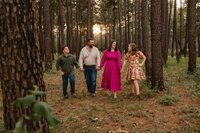 a family walks hand in hand in the pine trees during their family photo session in conroe,texas.