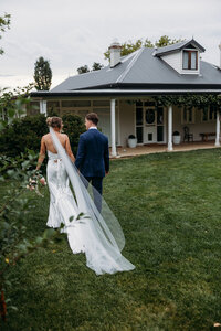 Bride and groom holding hands and walking in front of the homestead at Poachers Pantry, Springrange NSW