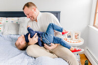 Dad and son laughing and playing together on a bed