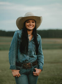 Senior portrait at Triple T Farms in Fruitdale, Alabama — waist-up, thumbs in pockets, smiling at
the camera.