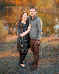 Husband and wife standing together by lake at golden hour during family photography session