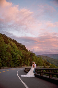 sunset wedding photos in the foothills captured by photographers in gatlinburg tn of couple eloping to gatlinburg as they embrace and lean on the railing with the mountains in the distance 