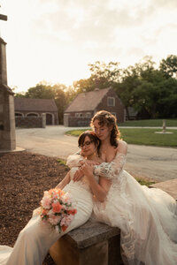 Newlyweds sitting on a curb as one leans back into the other