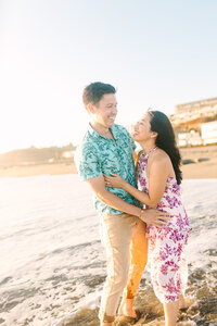 Engaged couple embrace on beach for engagement photos