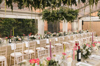 A beautifully set long dining table under a clear tent, adorned with elegant floral arrangements, candles, and draped greenery hanging from above. Chiavari chairs line the table, creating a sophisticated setting for a wedding at New Barn Farm.