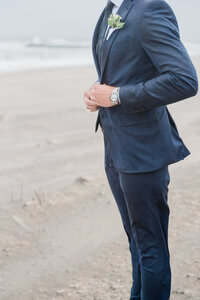 the groom buttoning his navy blue suit jacket, with the ocean in the background