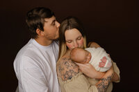 Family portrait of parents embracing their newborn baby with warm expressions. Photographed by Inland Empire newborn photographer Kaitlyn Dawn Photography.