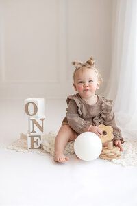 One year old baby girl wearing a brown romper for her milestone session in South Central Minnesota.