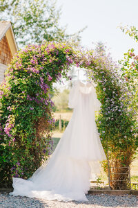 Wedding dress hanging in between a green floral arch