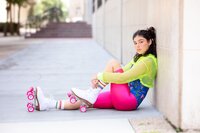 Tween girl wearing neon green mesh and bright pink leggings sitting against a wall in white roller skates during an urban photo session. (Photographed by Nature's Child Photography)