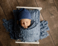 Sleeping newborn baby boy wrapped in a blue swaddle and posed in a rustic wooden bed prop during a studio newborn photography session by Inland Empire newborn photographer Kaitlyn Dawn Photography.