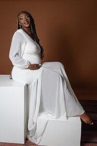 A woman in a white dress sits gracefully on a wooden box, enjoying a moment of calm and reflection.