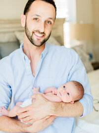 Father holding his newborn baby in natural window light during an in-home lifestyle newborn photography session.