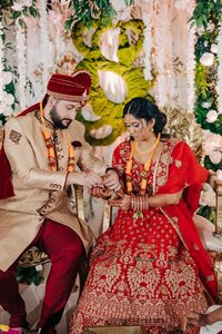 Bride and groom in traditional indian wedding attire performing a ritual at their ceremony, surrounded by floral decorations.