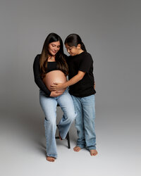 Expecting mom seated with her child gently touching her belly, sharing a tender pregnancy moment during a maternity session by Kaitlyn Dawn Photography in Yucaipa.