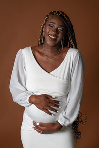 A pregnant woman in a white dress striking a pose for a photo, showcasing her beautiful baby bump.