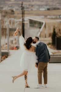 Bride and groom kissing on a city street, bride raising her arm playfully