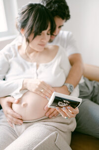 Expecting couple looking at ultrasound together during in home Miami maternity photoshoot