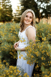 High school senior girl standing among yellow flowers during golden hour, outdoor senior portrait by Kaitlyn Dawn Photography.