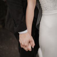 Mains enlacées d'un couple marié, détail de la robe blanche et du costume noir