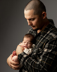 Father holding his sleeping newborn baby during a heartfelt studio newborn portrait session by Kaitlyn Dawn Photography.