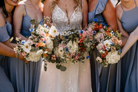 The bride and bridesmaids hold their bouquets together. The bouquets are made of poppies, eucalyptus, peonies, and baby's breath.