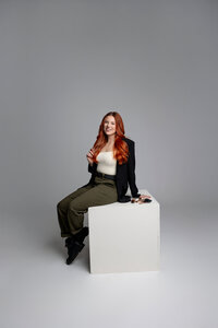 Professional branding portrait of red-haired woman seated on white cube, smiling. Photograph by Yucaipa branding photographer Kaitlyn Dawn Photography
