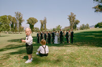 Two toddlers in front of wedding party posing outdoors on lawn