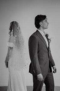 Mariés dos à dos sur fond neutre, voile fleuri translucide et boutonnière florale, portrait épuré en studio au Studio Giovanelli