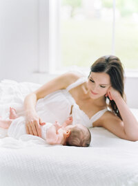 Mother snuggling baby on white sheets during Denver Newborn Photo Session/