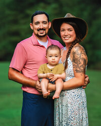 Mother and father holding their baby son in a wooded setting during an outdoor family photography session in Eastern North Carolina