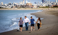 Family of four holding hands on the beach with the city of san francisco in the background