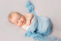 Sleeping baby boy wrapped in soft blue fabric during New Bern newborn photography session