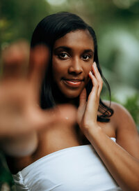 Senior portrait at Bella Sera Gardens in Loxley, Alabama — headshot reaching toward the
camera with one hand, the other hand on her face.