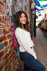 High school senior girl posing by a brick alley wall in an urban setting, senior portrait by Kaitlyn Dawn Photography.