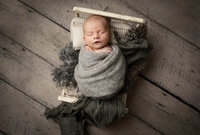 Baby boy wrapped in grey wrap on small white bed