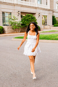 Senior girl wearing white dress strolling toward the camera smiling