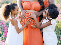 A closeup of dad and daughters caressing mom's pregnant belly